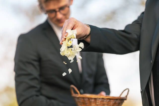 Trauergäste werfen Blumenblüten auf das Grab